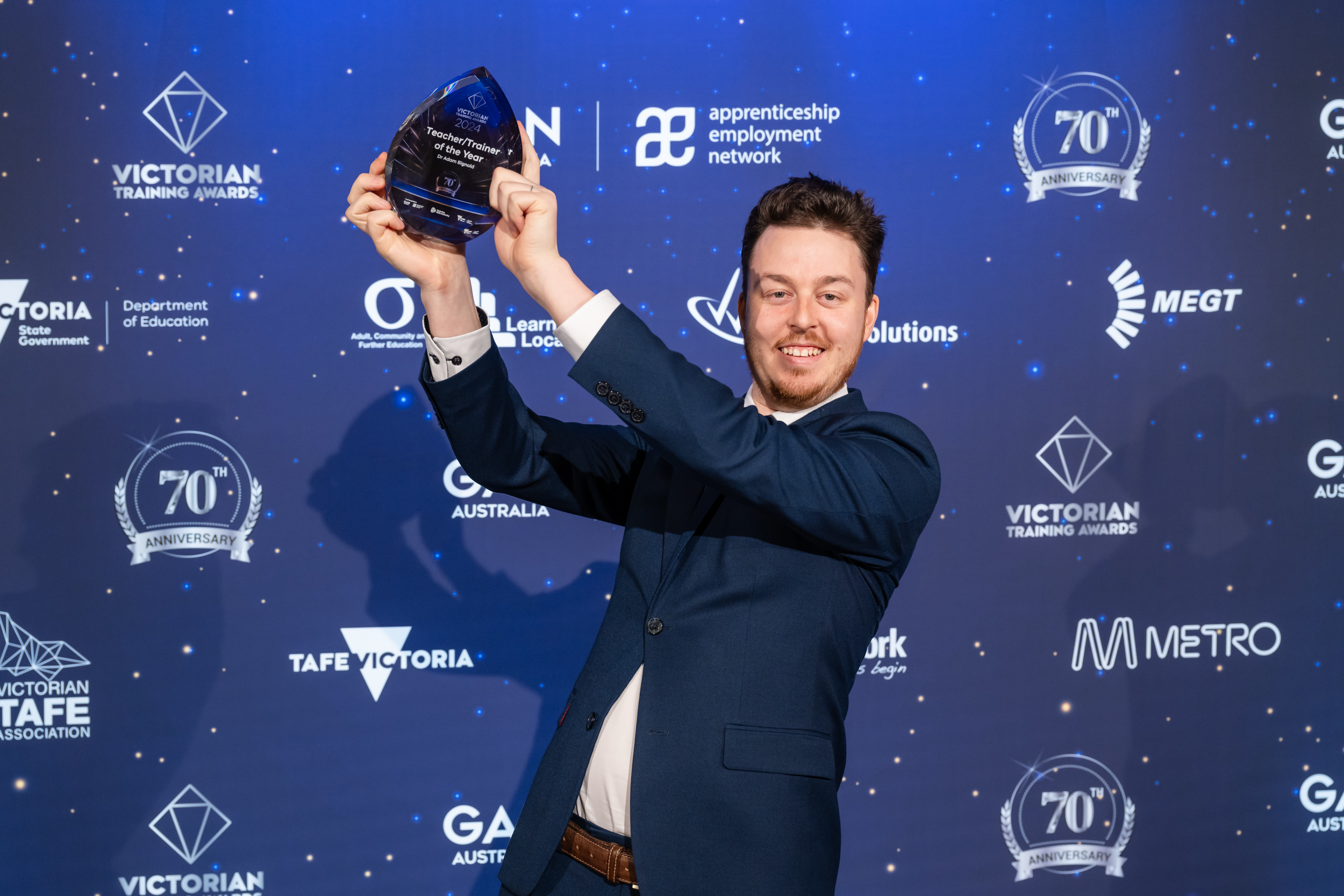 Young man smiling and holding up his award in front of media wall